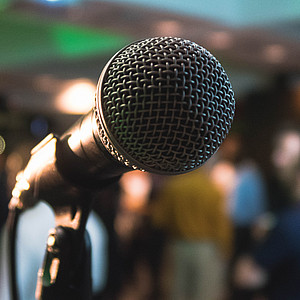 Bild eines Mikrofons vor unscharf gestelltem Hintergrund einer Veranstaltung