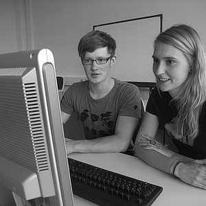 Schwarz/ weiß Foto von einem Mann und einer Frau, die zusammen an einem Computer sitzen.