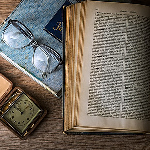 Foto von aufgeschlagenem Buch neben Brille und Taschenuhr
