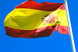 zu sehen ist die Spanische Flagge im Wind wehend vor blauem Himmel 