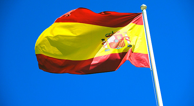 zu sehen ist die Spanische Flagge im Wind wehend vor blauem Himmel 