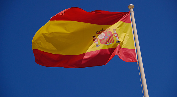 zu sehen ist die Spanische Flagge im Wind wehend vor blauem Himmel 