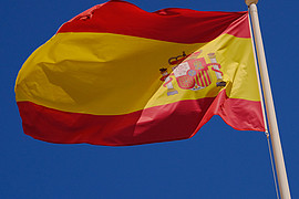 zu sehen ist die Spanische Flagge im Wind wehend vor blauem Himmel 