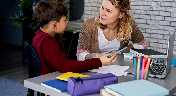 eine lächelnde Lehrkraft erklärt einem Kind Aufgaben 