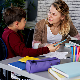 eine lächelnde Lehrkraft erklärt einem Kind Aufgaben 