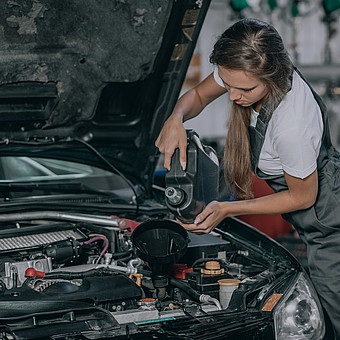 Eine junge Studierende prüft den Ölstand eines Fahrzeugs in einer Werkstatt 