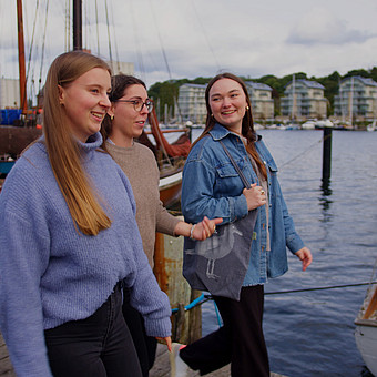 drei Studierende der Europa Univeristät Flensbrug gehen am Museumshafen von Flensburg entlang und unterhalten sich.