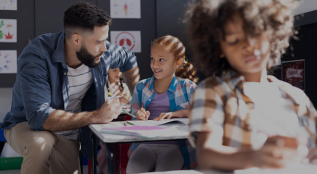 eine Lehrkraft und ein lächelndes Mädchen das im Unterricht am Tisch arbeitet