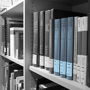 Schwarz/ weiß Bild von Bücherregal in Bibliothek mit blau akzentuierten Büchern.