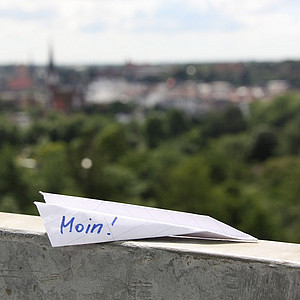 Bild von einem Papierflugzeug, das auf einer Mauer liegt und auf dem "moin" steht.