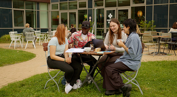 Gruppe an Studierender sitzen an einem Tisch und mit Laptop und Kaffee.