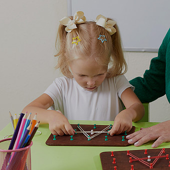 ein Kind sitzt an einem grünen Tisch und macht Übungen 