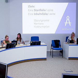 Bild zeigt Menschen an einem halbrunden Computertisch in einem Konferenzraum