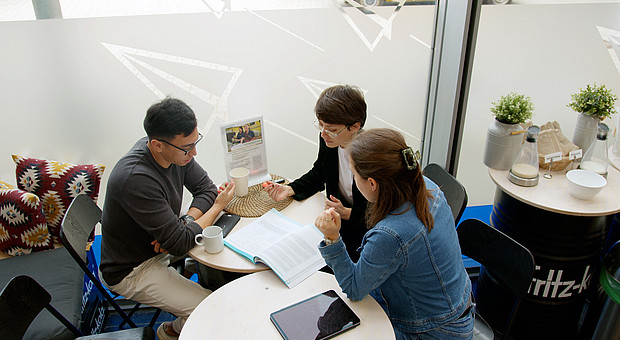 Gruppenarbeit von Studierenden an einem weißen Tisch in der Mensa der Europa Universität Flensburg.