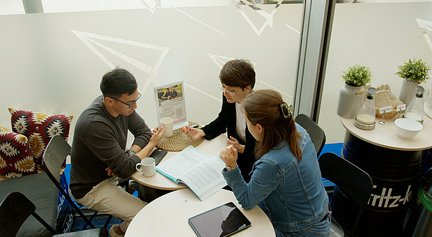Gruppenarbeit von Studierenden an einem weißen Tisch in der Mensa der Europa Universität Flensburg.