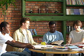 eine gemischte Gruppe Studierender sitzt an einem Tisch und diskutiert Fachliteratur 