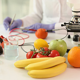 Verschiedene Obst Sorten liegen neben einem Mikroskop auf einem Tisch 