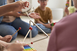 Kinder sitzen mit Studierenden auf dem Boden und testen Instrumente aus 