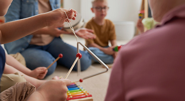 Kinder sitzen mit Studierenden auf dem Boden und testen Instrumente aus 