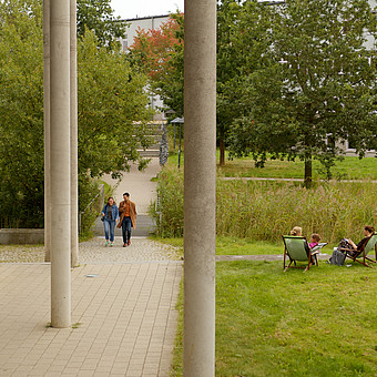 Zwei Menschen laufen am Audimax vorbei.