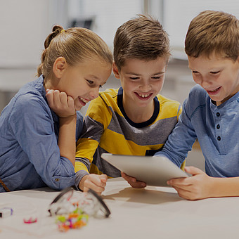 eine Gruppe lächelnder Kinder mit Tablet im Klassenraum 