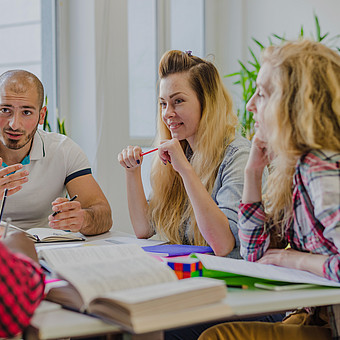 Eine Gruppe Studierender sitzt an einem Tisch und löst gemeinsam Aufgaben. 
