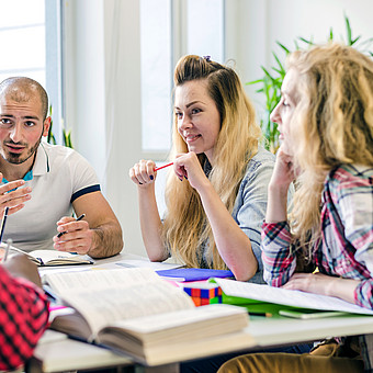 Eine Gruppe Studierender sitzt an einem Tisch und löst gemeinsam Aufgaben. 