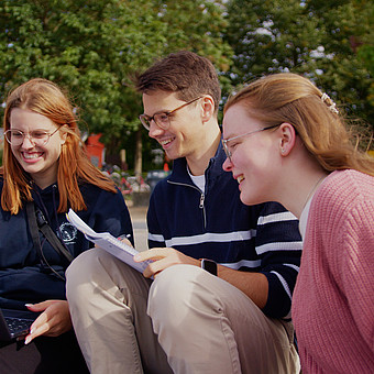 Drei Studierende sitzen mit Lernzetteln an der Hafenspitze in Flensburg 