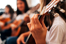 zeigt eine Person mit rotem T-Shirt von hinten, der Gitarrenhals ist links oben zu sehen. 