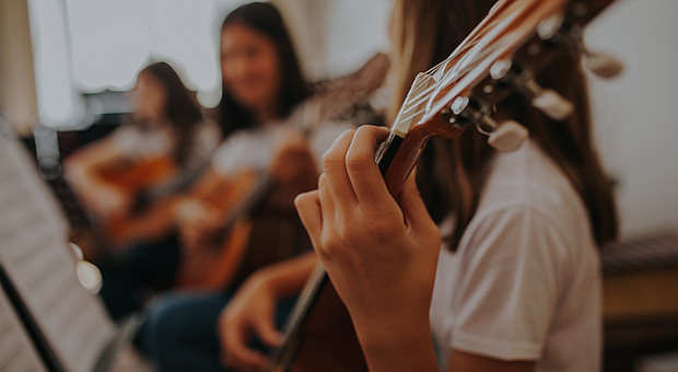 zeigt eine Person mit rotem T-Shirt von hinten, der Gitarrenhals ist links oben zu sehen. 