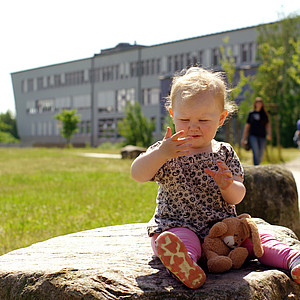 Bild von Kleinkind auf einem Stein vor der Bücherei