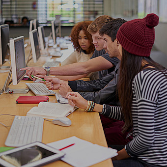 Eine Gruppe von Studierenden sitzen mit Computer in der Bibliothek 