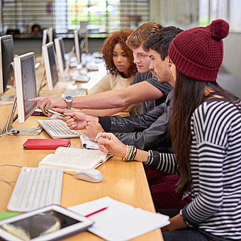 Eine Gruppe von Studierenden sitzen mit Computer in der Bibliothek 