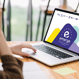 Eine Studentin sitzt an einem Notebook, auf dem Bildschirm ist das Logo des "EMERGE"-Projekts zu sehen