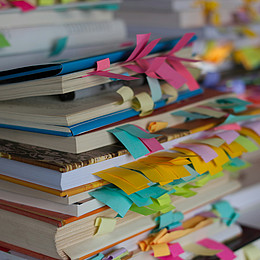 Mehrere Bücher, die mit bunten Postits versehen sind, liegen übereinander auf einem Stapel