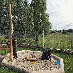 Foto vom Aussenspielbereich der Mattisburg mit Sandkasten und 2 spielenden Kindern