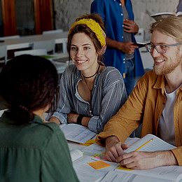 Vier Studierende sitzen gemeinsam an einem Tisch und tauschen sich aus. 