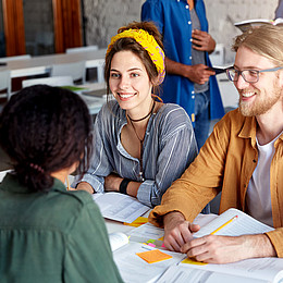 Vier Studierende sitzen gemeinsam an einem Tisch und tauschen sich aus. 