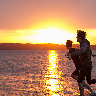 2 Freunde laufen bei Sonnenuntergang durchs flache Wasser am Strand