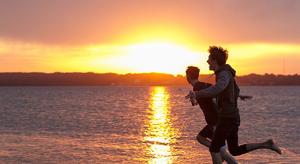 2 Freunde laufen bei Sonnenuntergang durchs flache Wasser am Strand