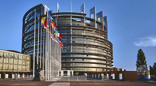 eine Weitaufnahme des Europa Parlaments, es wehen die Flaggen der EU Mitglieder in der Luft 