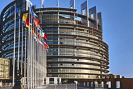 eine Weitaufnahme des Europa Parlaments, es wehen die Flaggen der EU Mitglieder in der Luft 