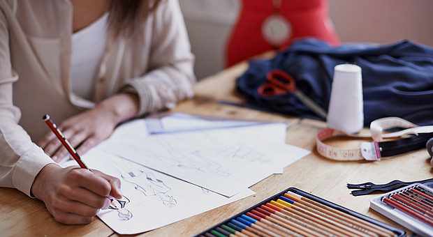 eine junge Designerin zeichnet an einem braunen Schreibtisch an einem Modekonzept mit Bleistift 