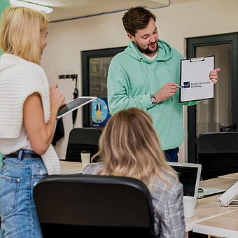 Eine Person im grünen Pullover erklärt Studierenden eine Theorie wöhrend eines Seminars 