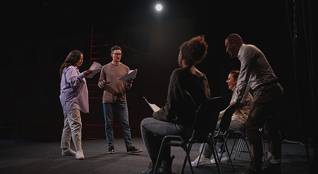 Vier Studierende und eine Dozierende Person befinden sich in einem Proberaumund proben für ein Theaterstück. 