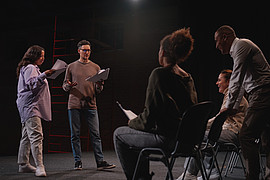 Vier Studierende und eine Dozierende Person befinden sich in einem Proberaumund proben für ein Theaterstück. 