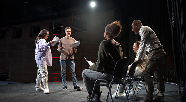 Vier Studierende und eine Dozierende Person befinden sich in einem Proberaumund proben für ein Theaterstück. 