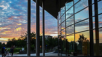 Außenansicht des Audimax. In der großen Fensterfront spiegelt sich der Sonnenuntergang.