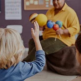 Nahaufnahme einer Rückenansicht von Kindern. Ein kleiner Junge mit erhobener Hand während Lehrkraft erklärt 