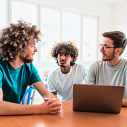 eine Gruppe von Studierenden sitzt in einem Seminarraum und diskutiert mit Laptop 